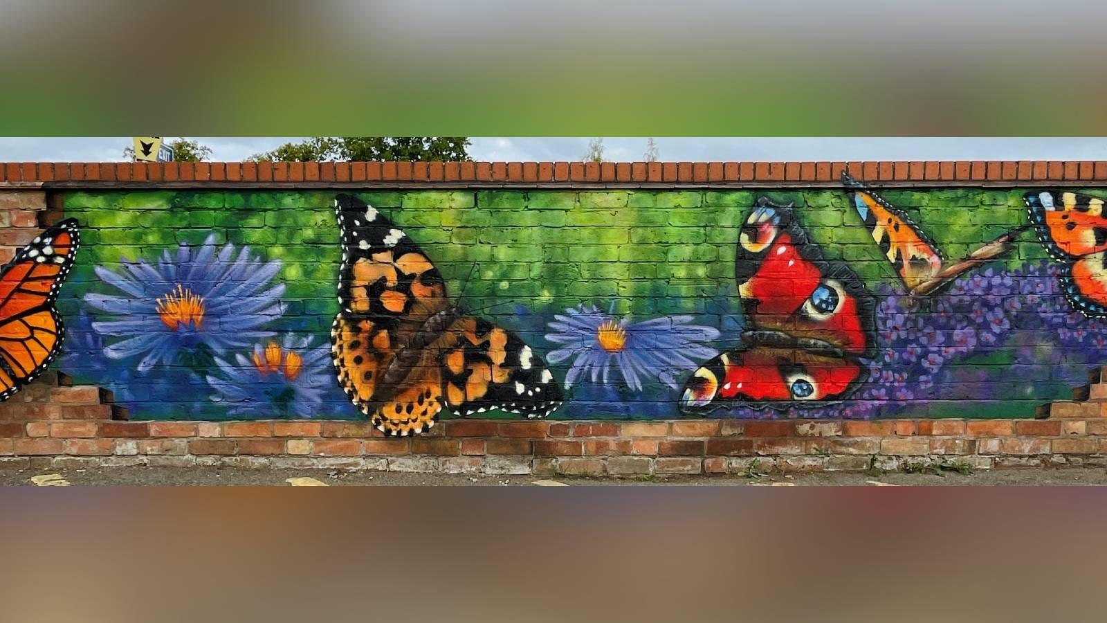 A red brick wall that has been painted over with large monarch butterflies and purple flowers.