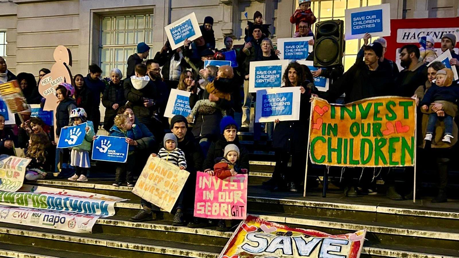 Campaigners on steps holding up placards that say "invest in our children" and "save our children's centres"