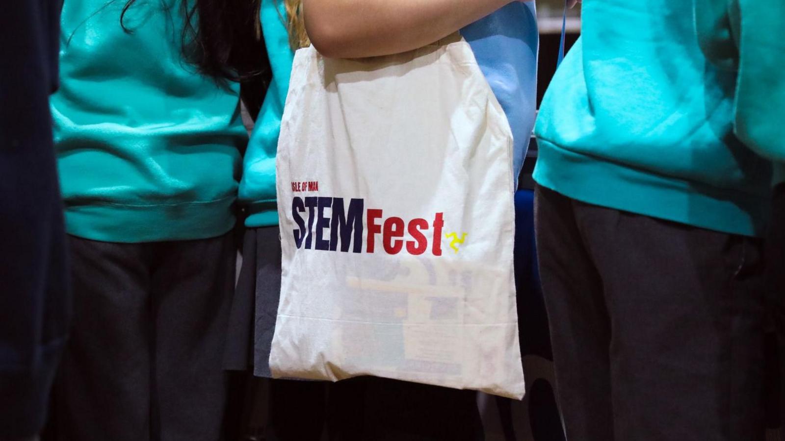 a closeup of a girl wearing a blue uniform shirt with a white canvas bag that reads STEMFest.