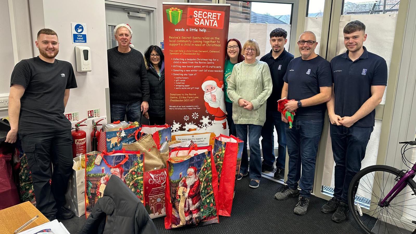 A group of volunteers stood up with bags of presents at their feet