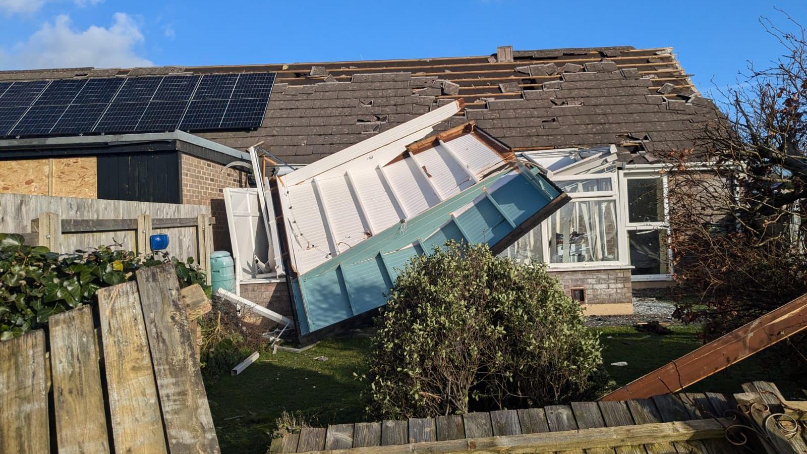 House with roof slates that have been blown off, and the roof of a conservatory