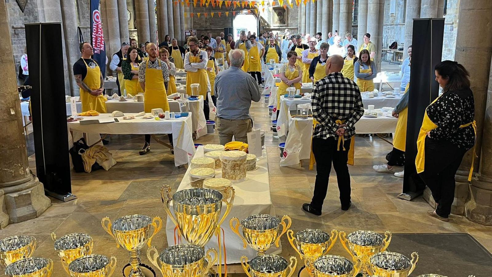 80 judges stand behind tables filled with cheese in a church 