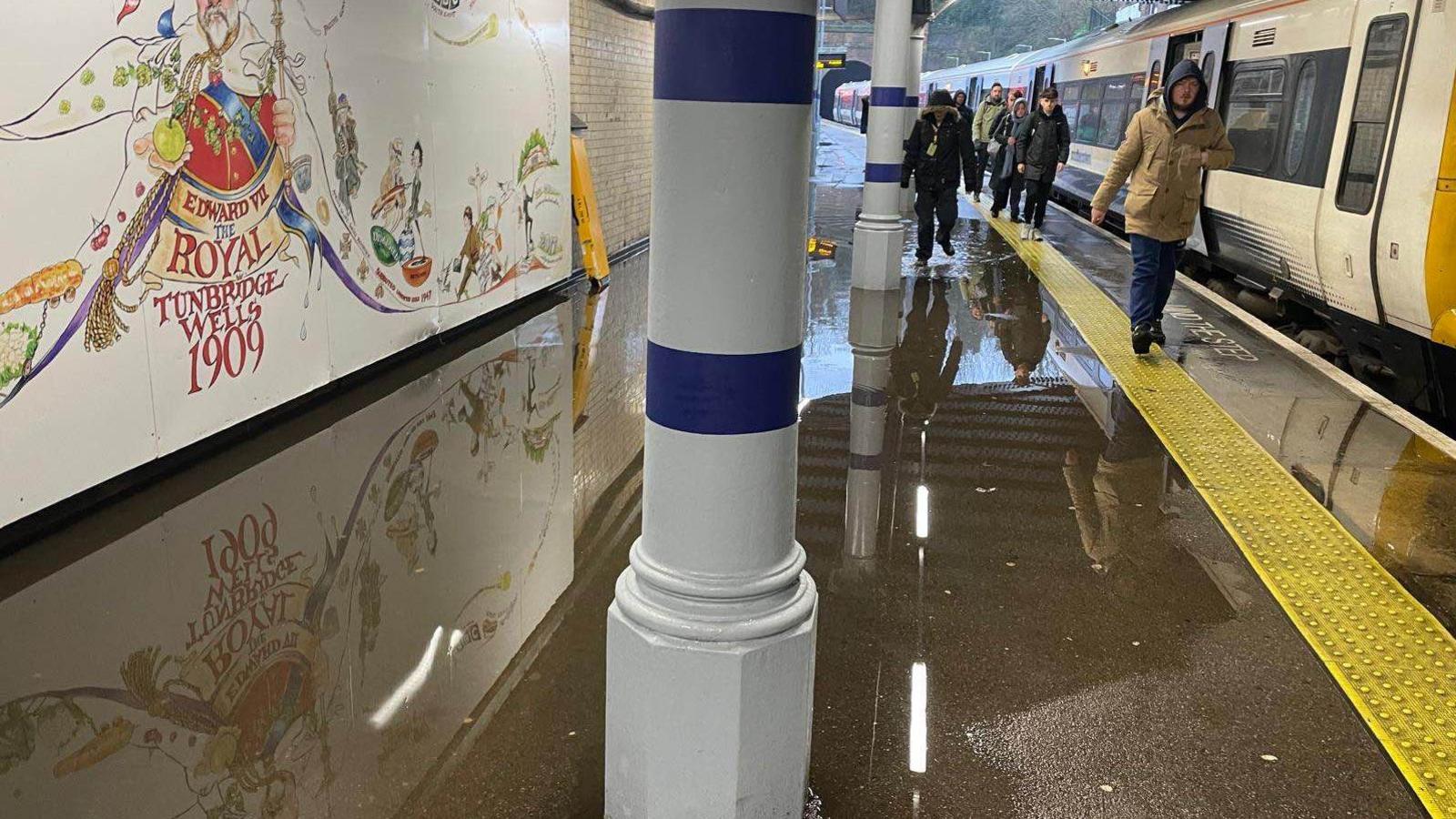 Passengers step off a train onto a flooded platform