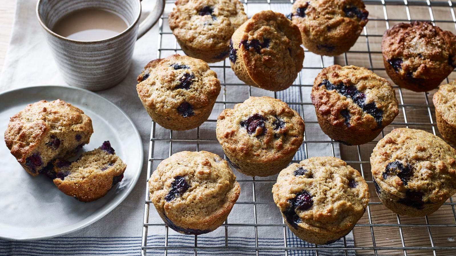Healthy blueberry muffins on a wire rack with one that's on a small plate and cut open. 