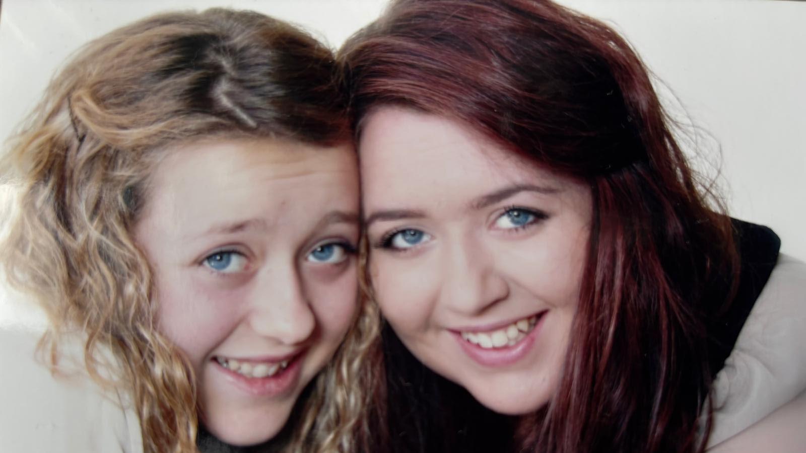 A young woman with blonde hair and a young woman with dark brown hair smiling