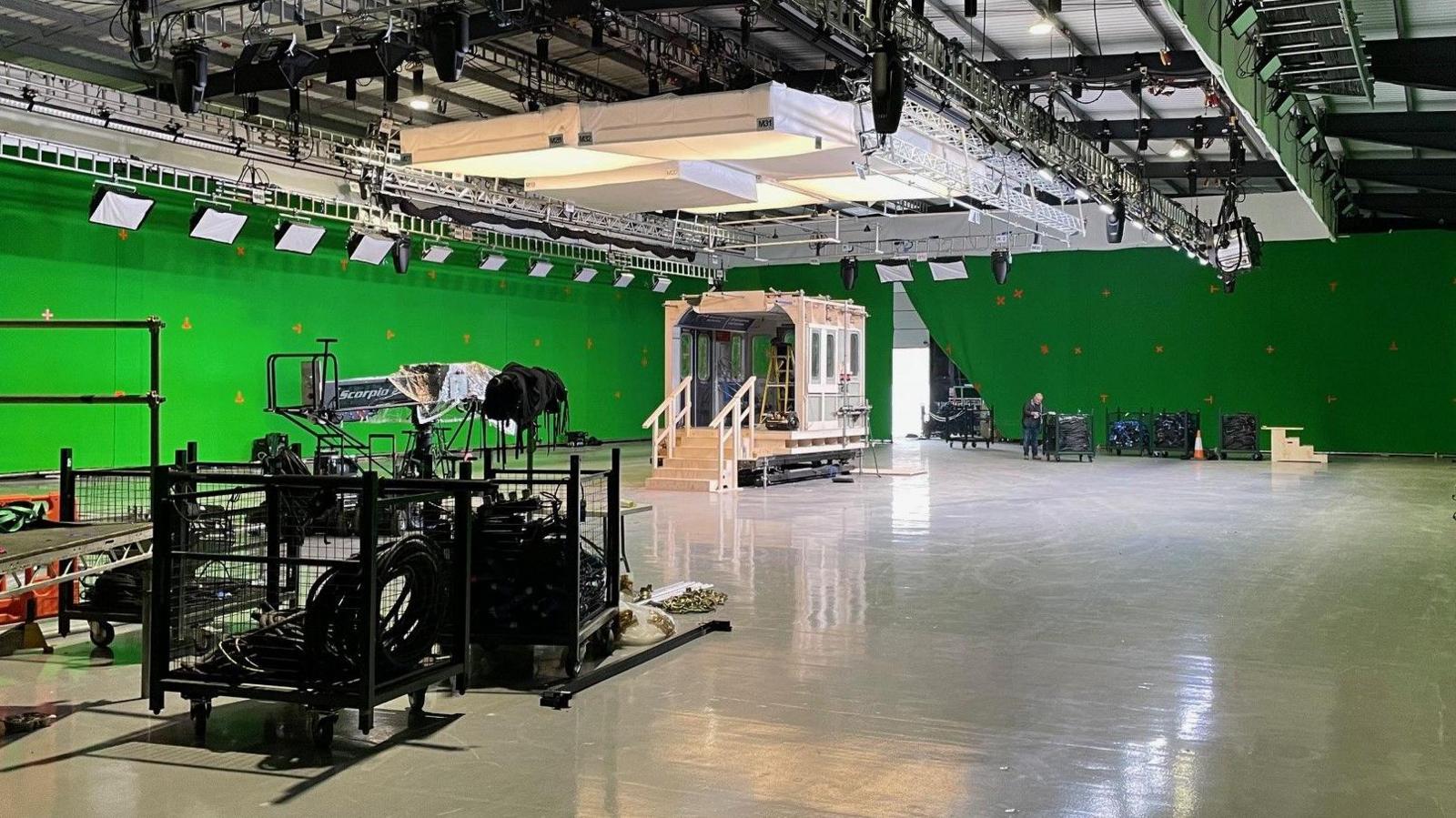 A large green-walled room, with a wooden train carriage in the middle. There are cameras pointing at it.