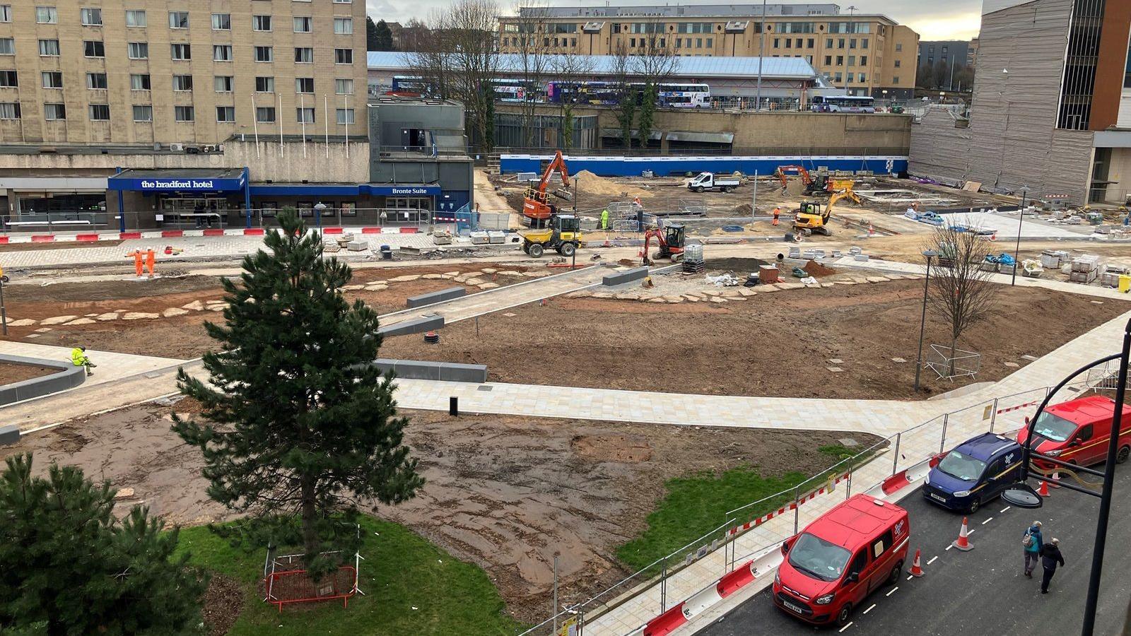 A view of an urban area being redeveloped into a park with green spaces and surrounded by red and whit barriers 