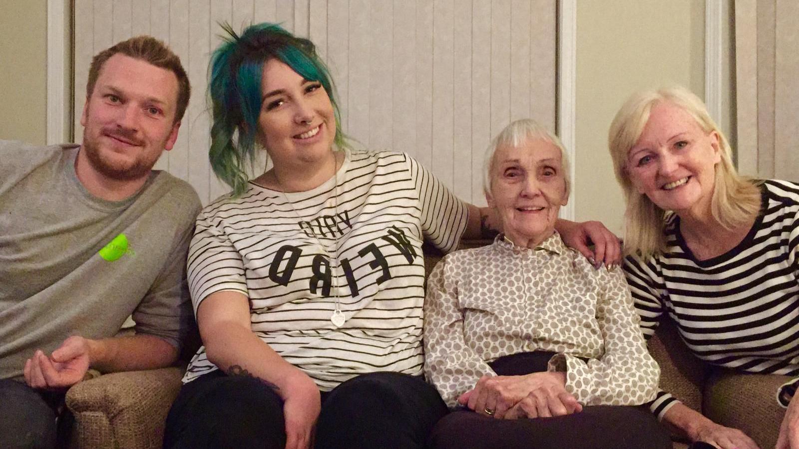 Anne with her grandchildren Andrew and Kirsty and daughter Gillian. They are sitting on a sofa and smiling.