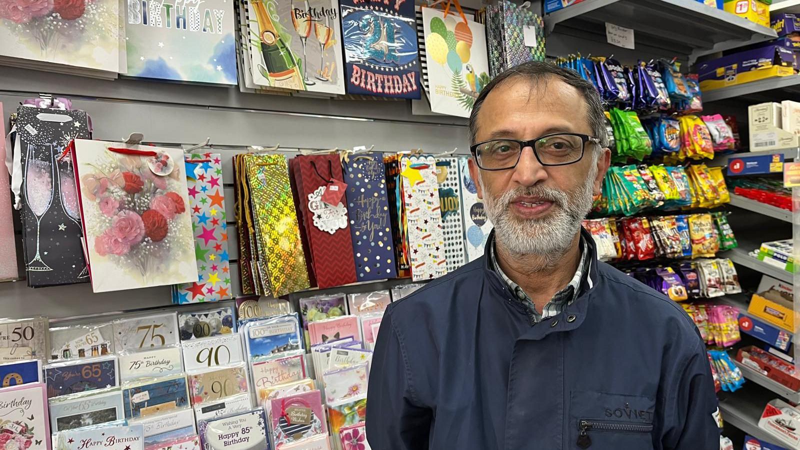 Muneer Memon - a man with a grey beard with cards and sweets behind him