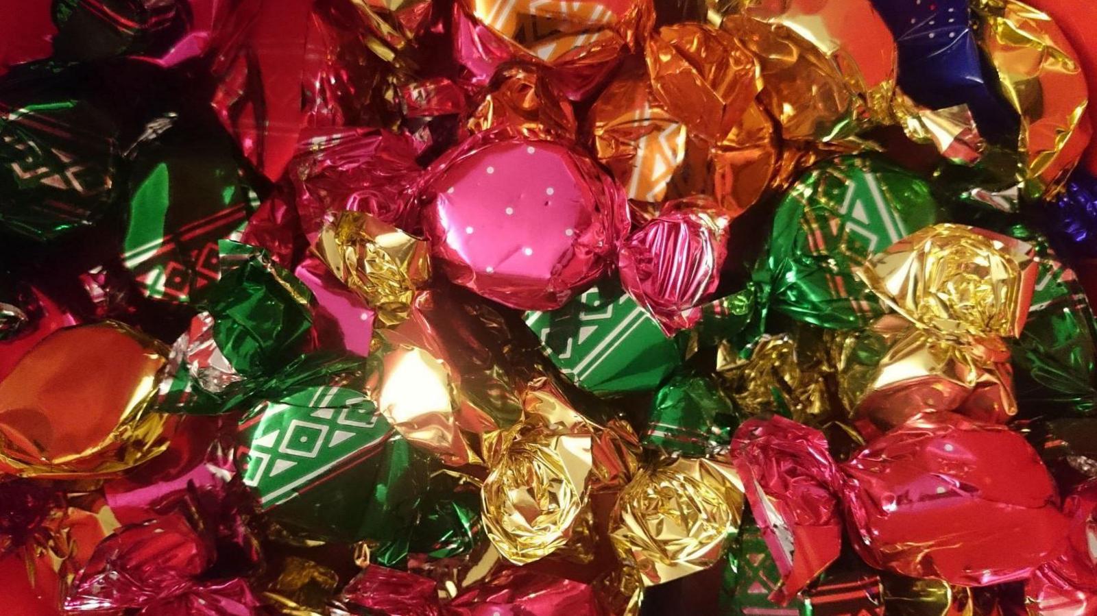 A full frame picture of foil-wrapped sweets in green, gold and orange wrappers.