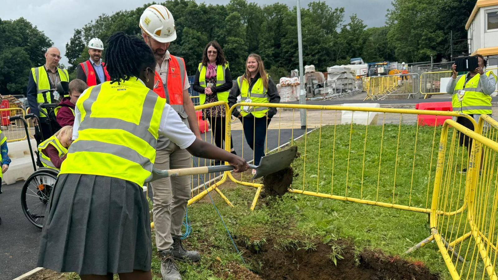 Image of people digging a hole in the ground to bury a time capsule. They are all wearing yellow high-vis jackets.