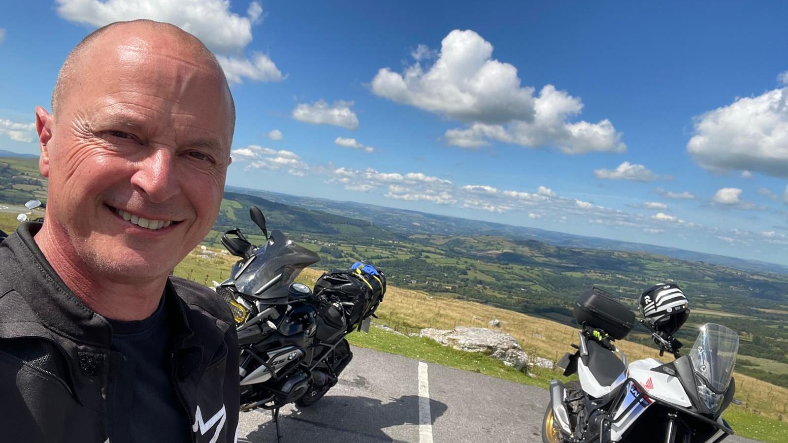 Julian Hall stood on a hill with two motorcycles