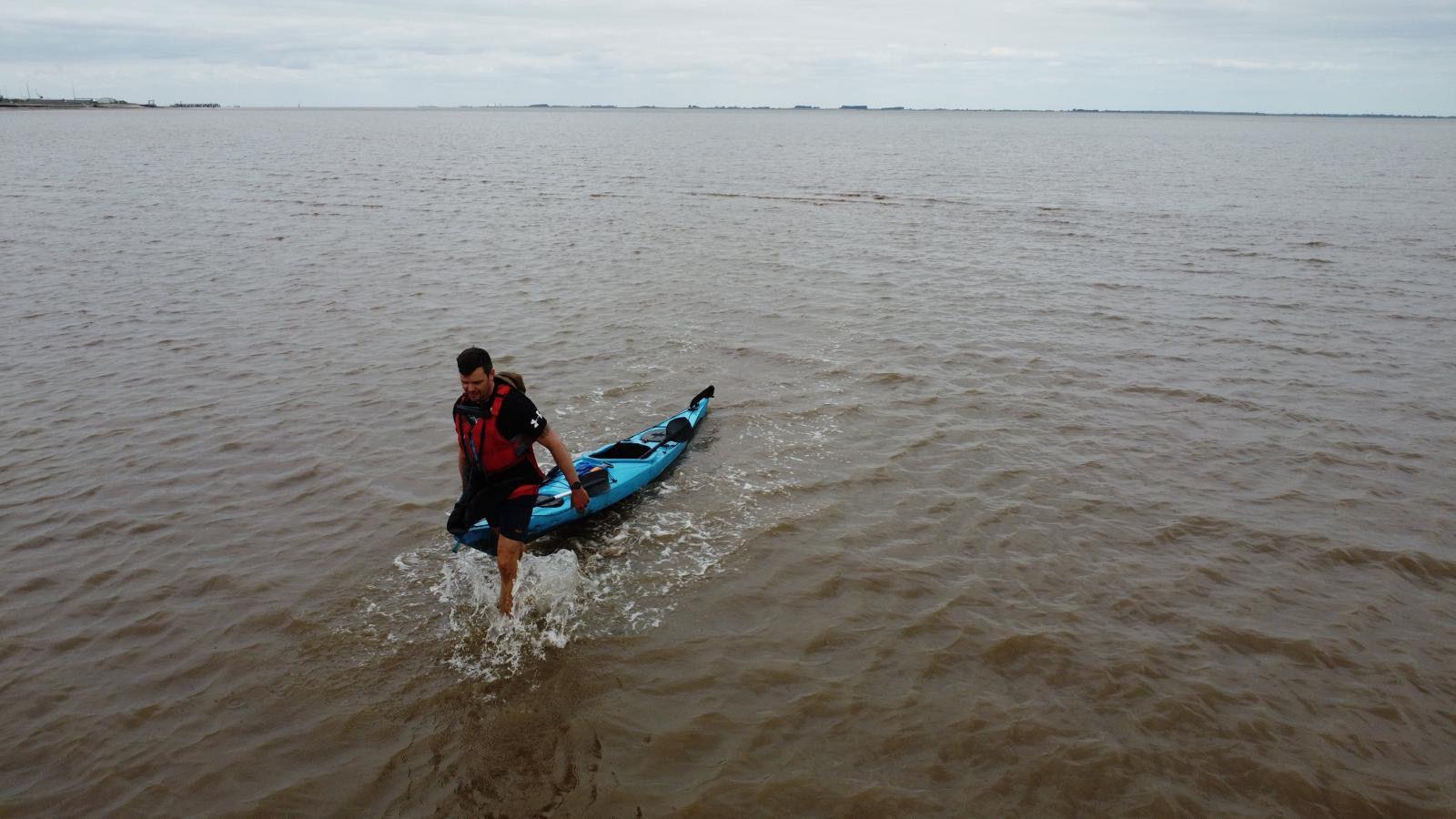 A man pulling his kayak ashore at the coast