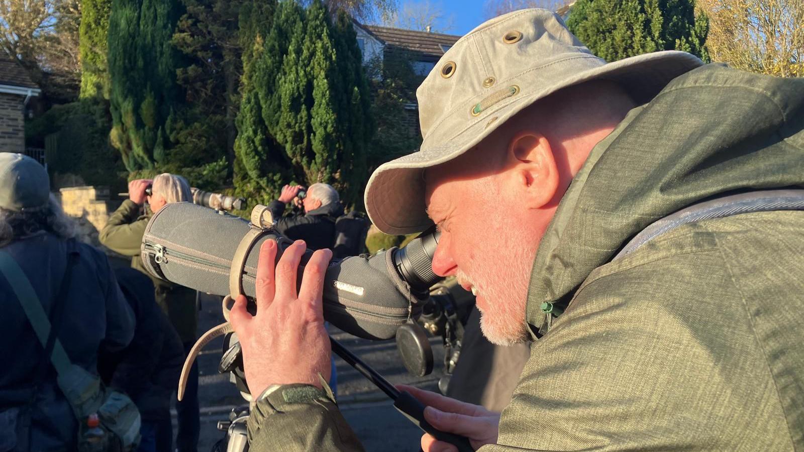 Paul, dressed in green, peers through a long lens to see the Scarlet Tanager.