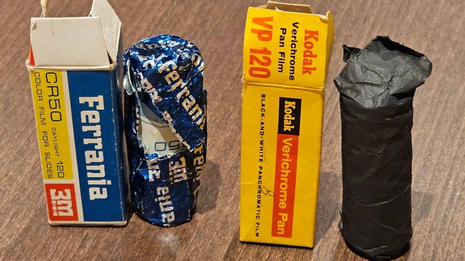 A close-up modern colour image of two 1960s rolls of photographic film, standing on a table alongside their boxes. On the left is a roll of Ferrania CR50 colour film for slides, and on the right is a roll of Kodak Verichrome Pan black-and-white panchromatic film.