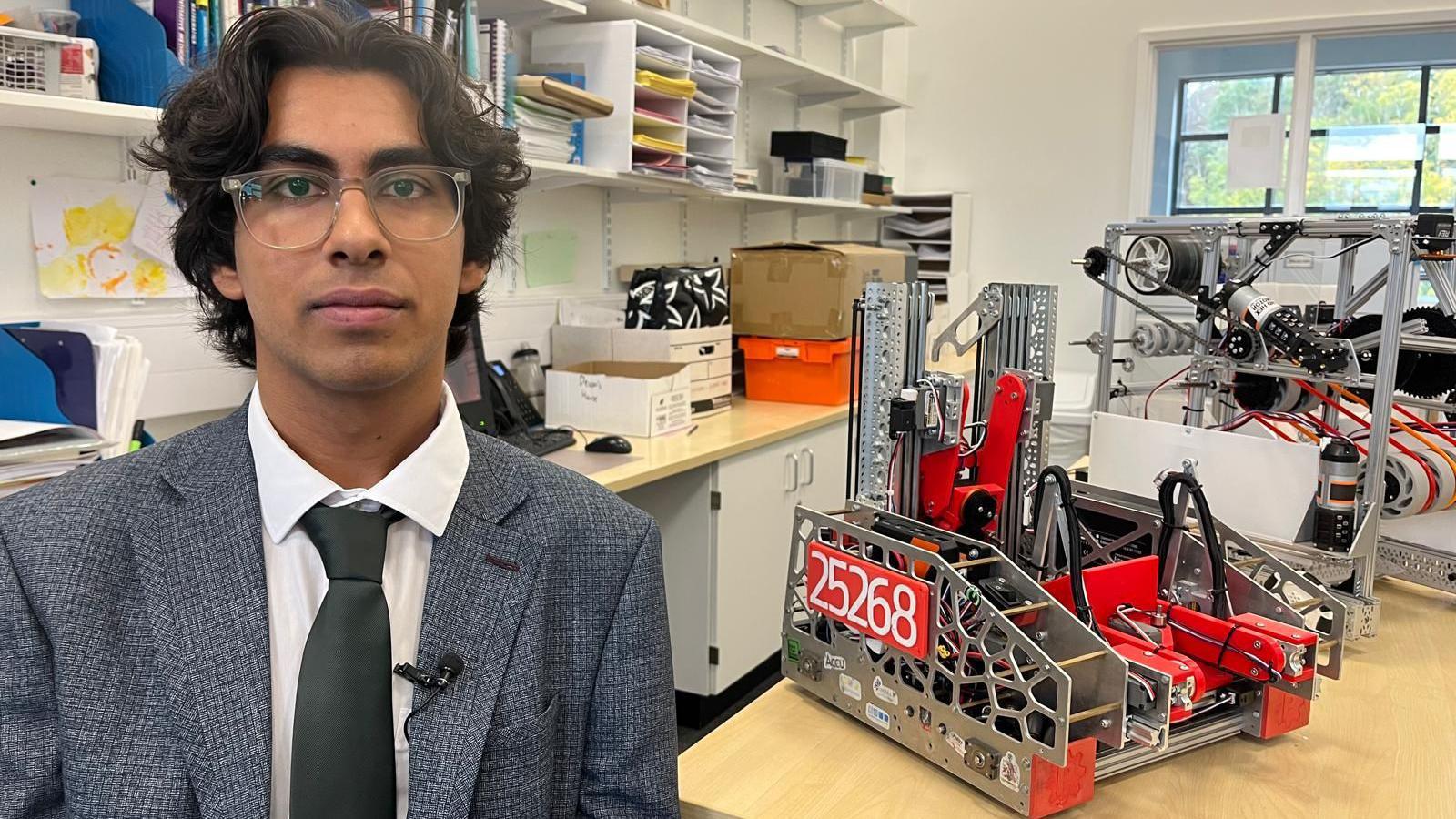 Adrian in a suit and tie sat next to a robot his team designed. It won them the national championships.