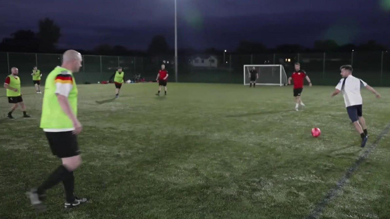 A group of men playing football on a floodlit pitch