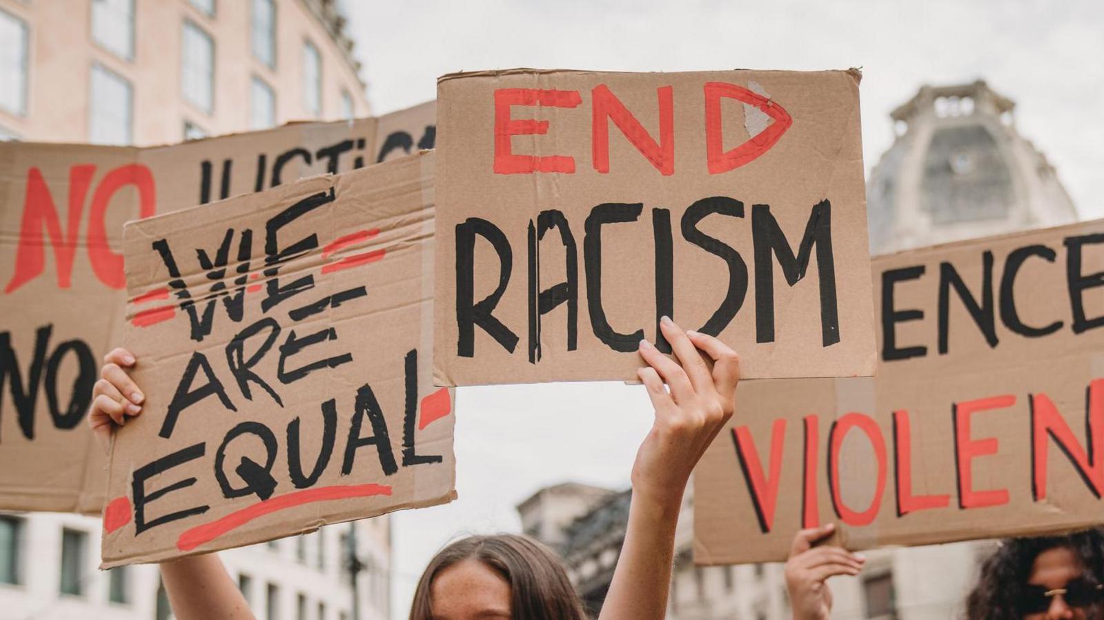 Signs being held aloft saying 'end racism' and 'we are equal'