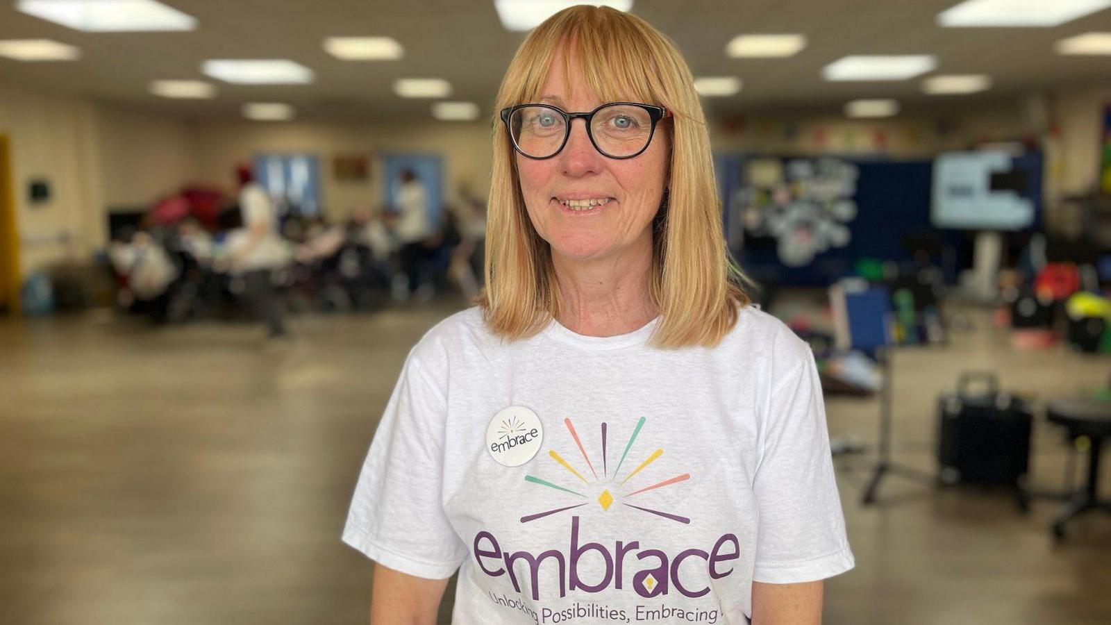 A woman with glasses wearing an embrace branded white tshirt