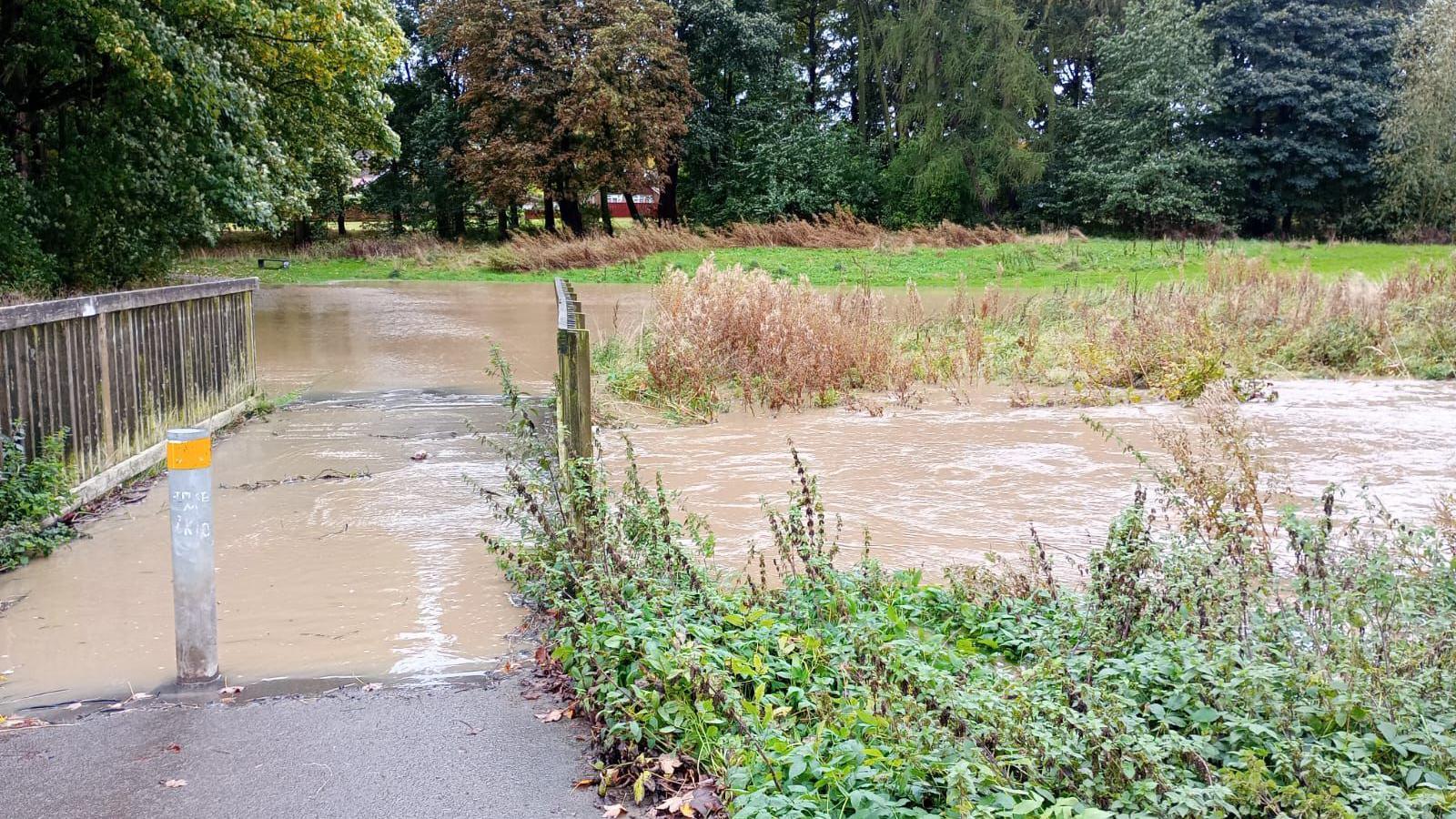 Cocker Beck Nature Reserve. A field and a small bridge are submerged by muddy flood water. 