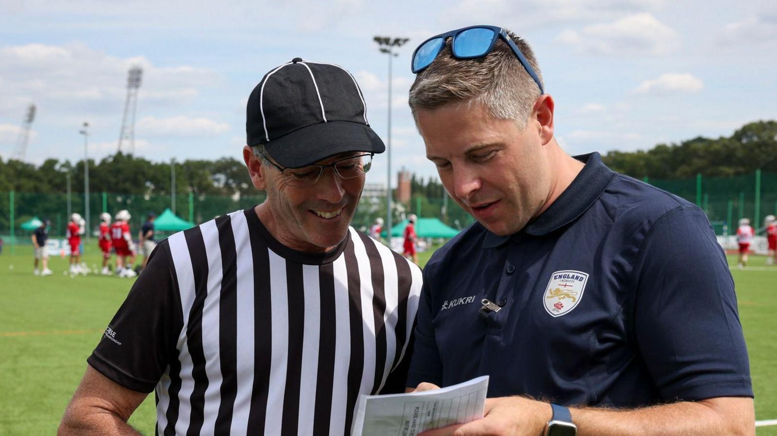 Michael Armstrong, in a navy blue England polo shirt, talking with a referee who is wearing a black and white striped t-shirt 