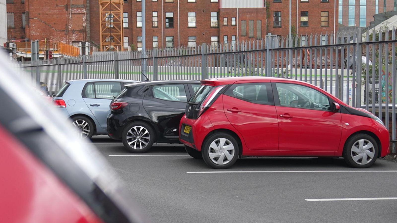 A car park in Belfast city centre. There are three cars parked in a row.