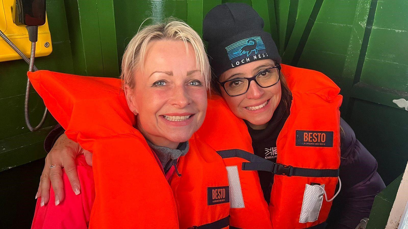 Dita Sanchez and a friend who are both wearing bright orange life jackets and smiling. 