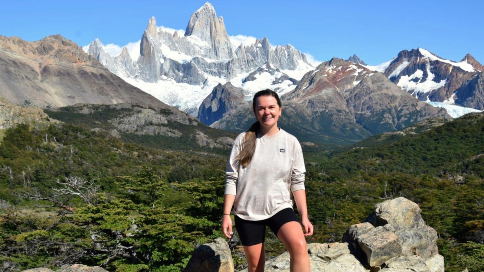 Rebecca O'Malley standing with mountains in the background. She wears shorts and a grey jumper.