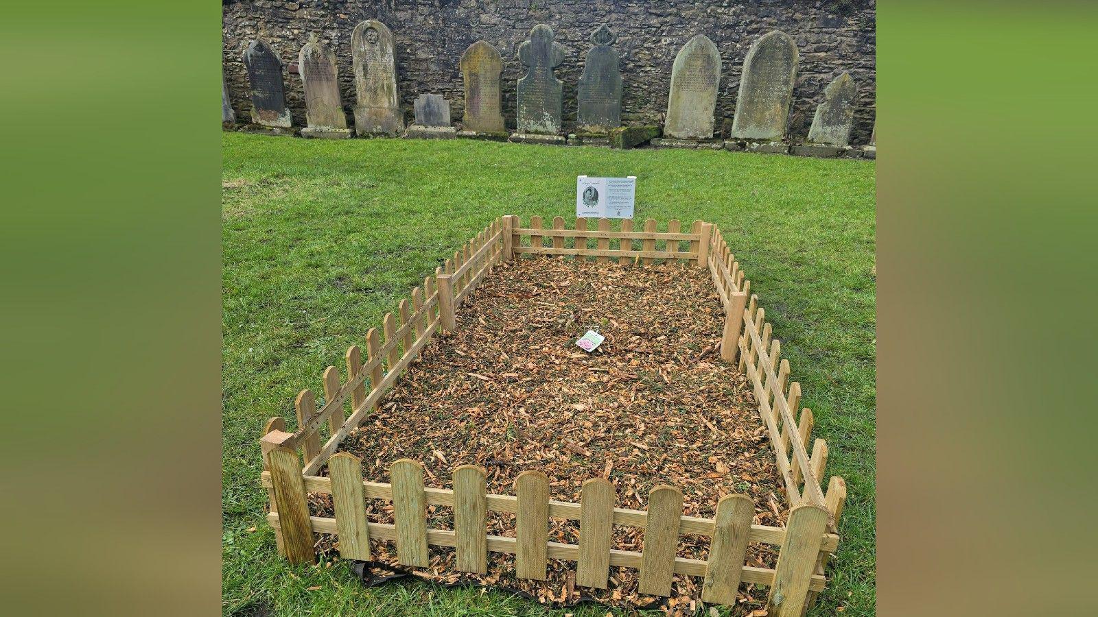 A short wooden fence surrounds the area of Lucy Sands' burial site, with a memorial plaque.