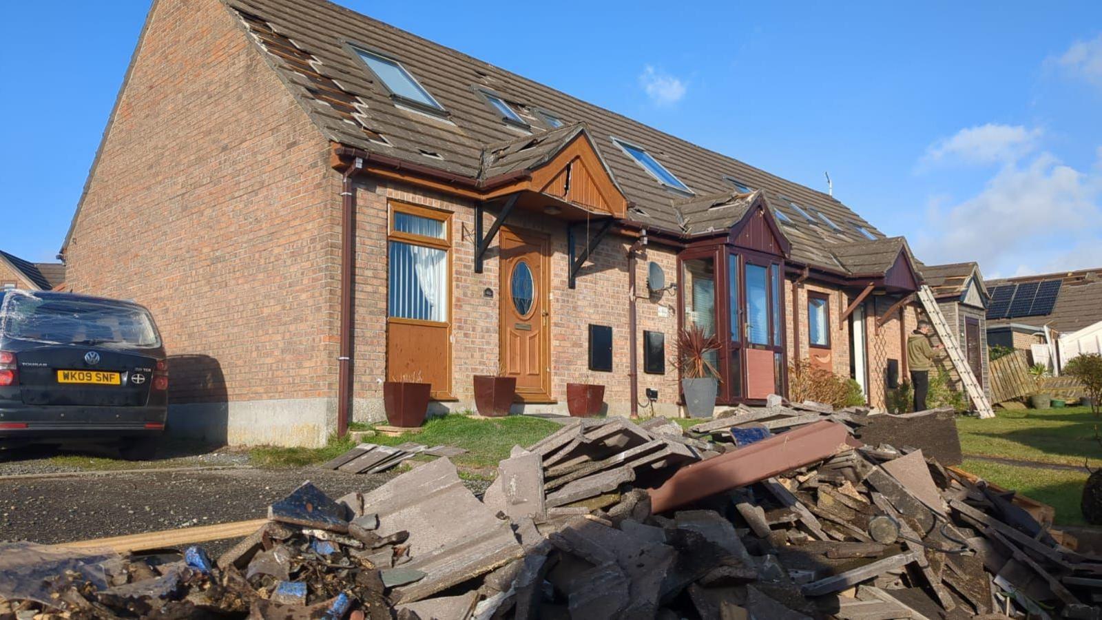 House with roof tiles missing, and tiles piled up in front