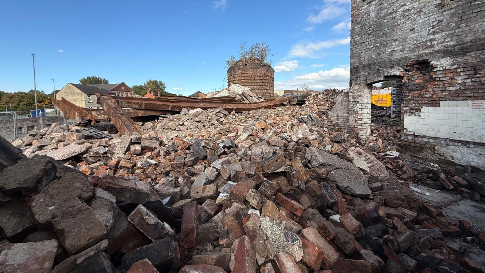 A pile of bricks, with a blue sky in the distance. There is part of a bottle-shaped kiln in the background of the image.