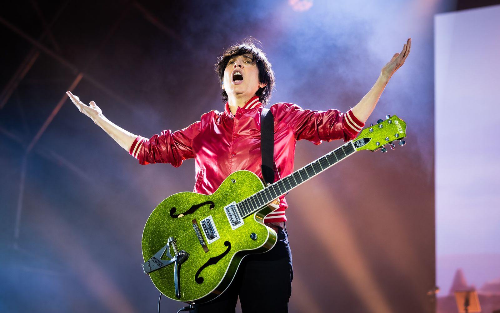 Texas lead singer Sharleen Spiteri on stage wearing a hot pink jacket with a lime green guitar worn on a strap and her arms outstretched