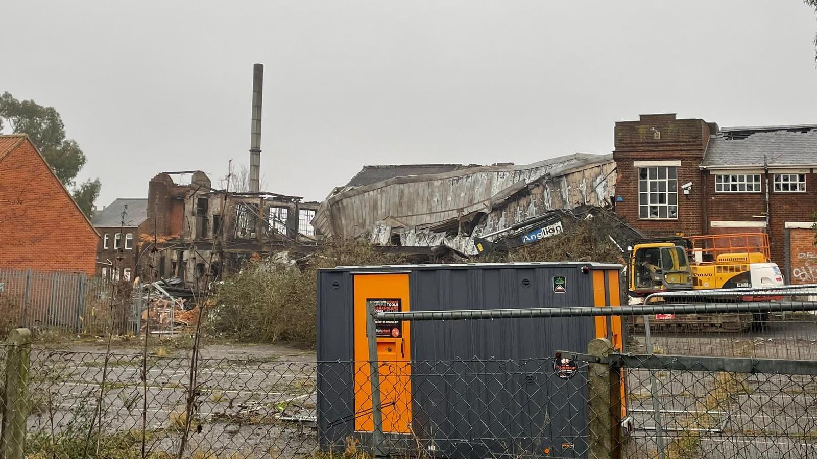 Demolition plant at the site of the former factory. Part of the roof has collapsed and the ruins can be seen in the background 