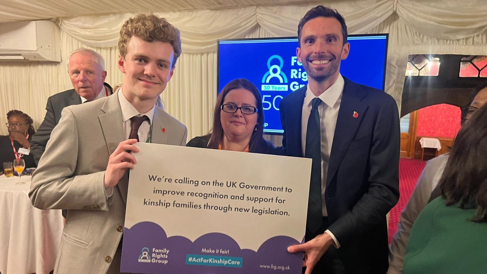 Sam Carling, Katy Cole and Josh MacAlister hold a sign which says: "We're calling on the UK government to improve recognition and support for kinship families through new legislation.'