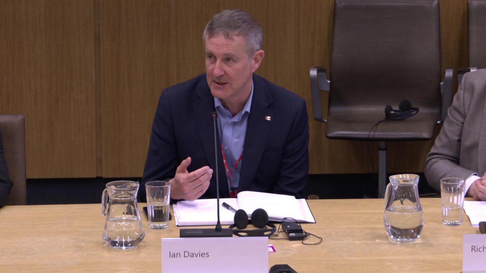 Ian Davies addressing the Economy Committee on Thursday. He has a notebook and pen on a table in front of him next too a jug and a glass of water.