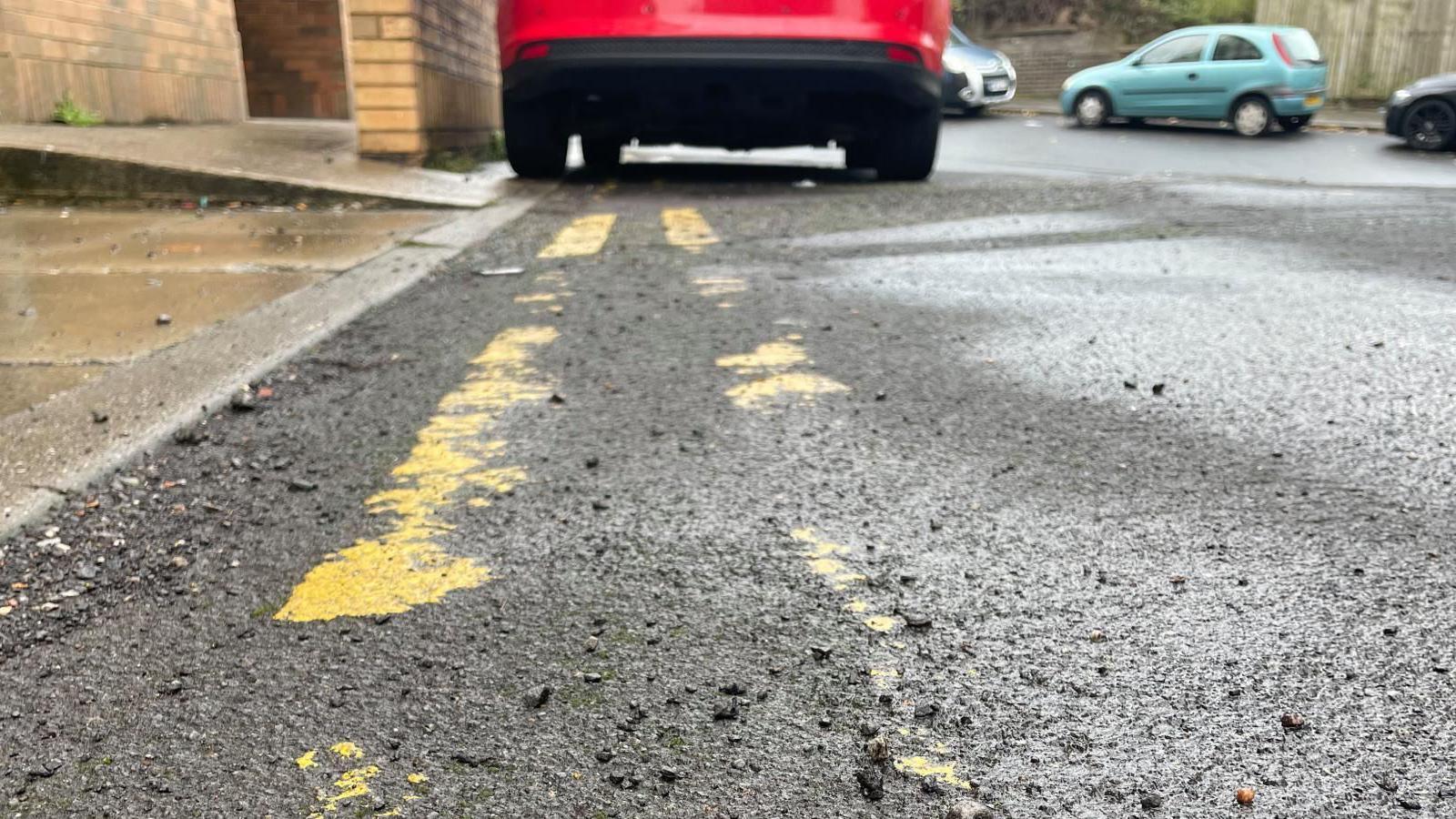 A red car is parked on faded double yellow lines