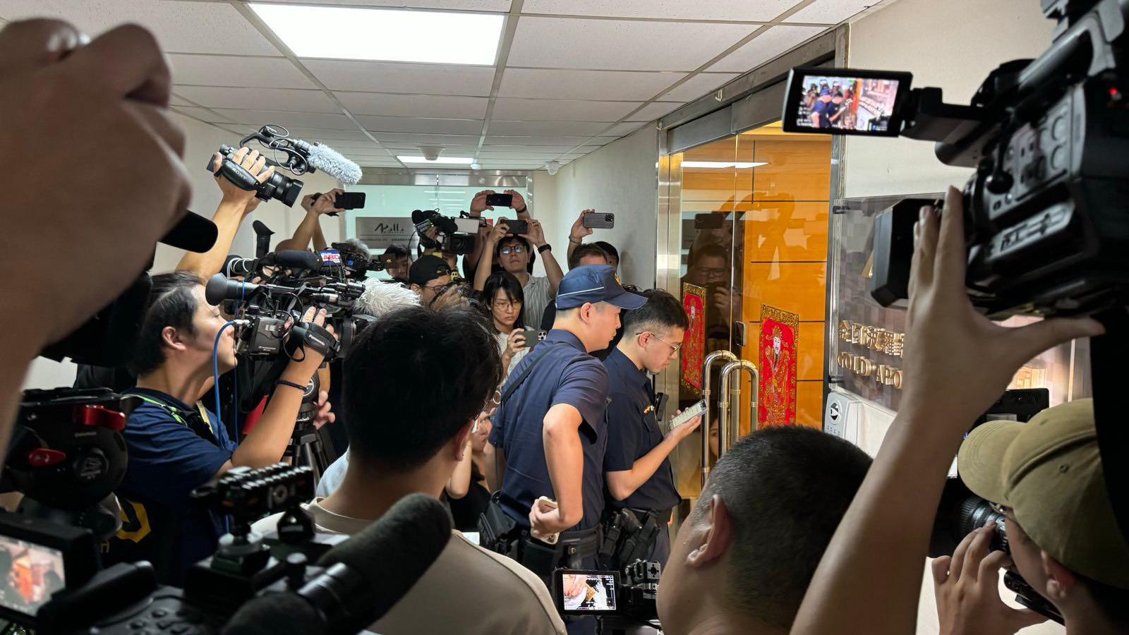 Reporters surround two police officers as they enter the offices of Gold Apollo in Taipei. 