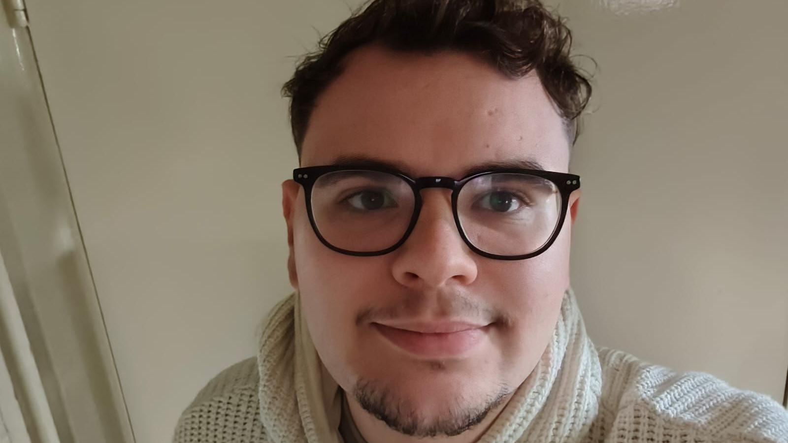 A selfie of Ethan Appleby. Ethan has short curly brown hair and a short goatee beard. He wears dark rimmed glasses and a cream pullover.