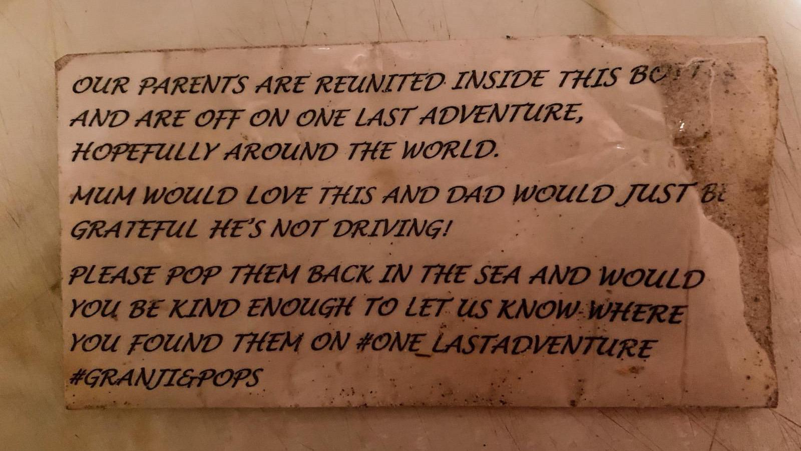A piece of paper that says "Our parents are reunited inside this bottle and are off on one last adventure, hopefully around the world. Mum would love this and Dad would just be grateful he's not driving! Please pop them back in the sea and would you be kind enough to let us know where you found them on #one_lastadventure #Granji&Pops."