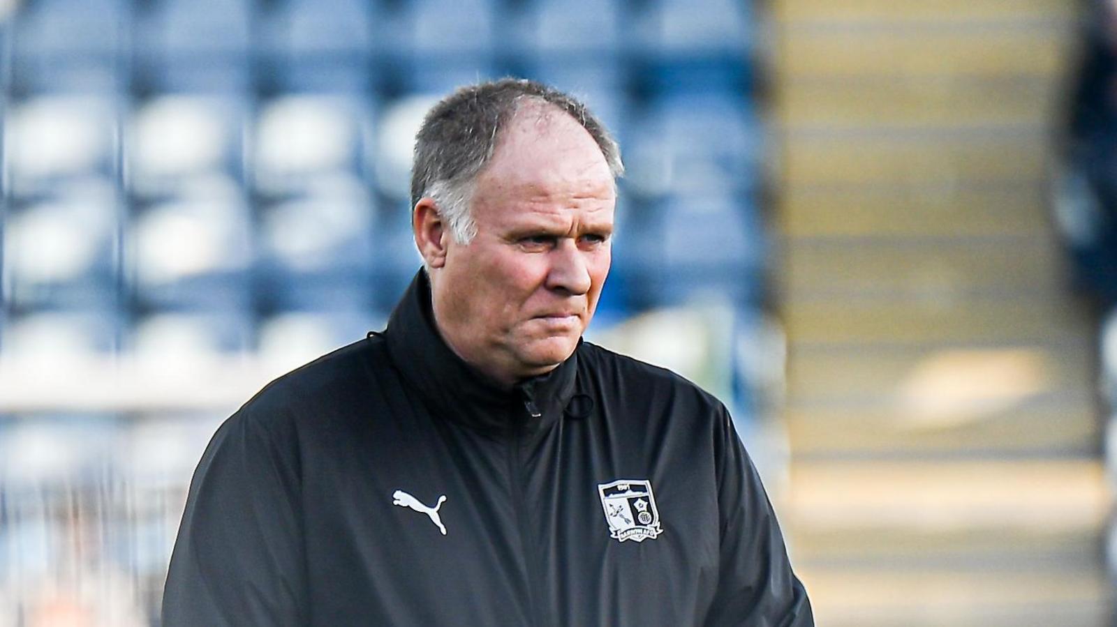 Neil McDonald, with his Barrow training coat zipped up to the top, stood watching his players warm up with a backdrop of blue seats 