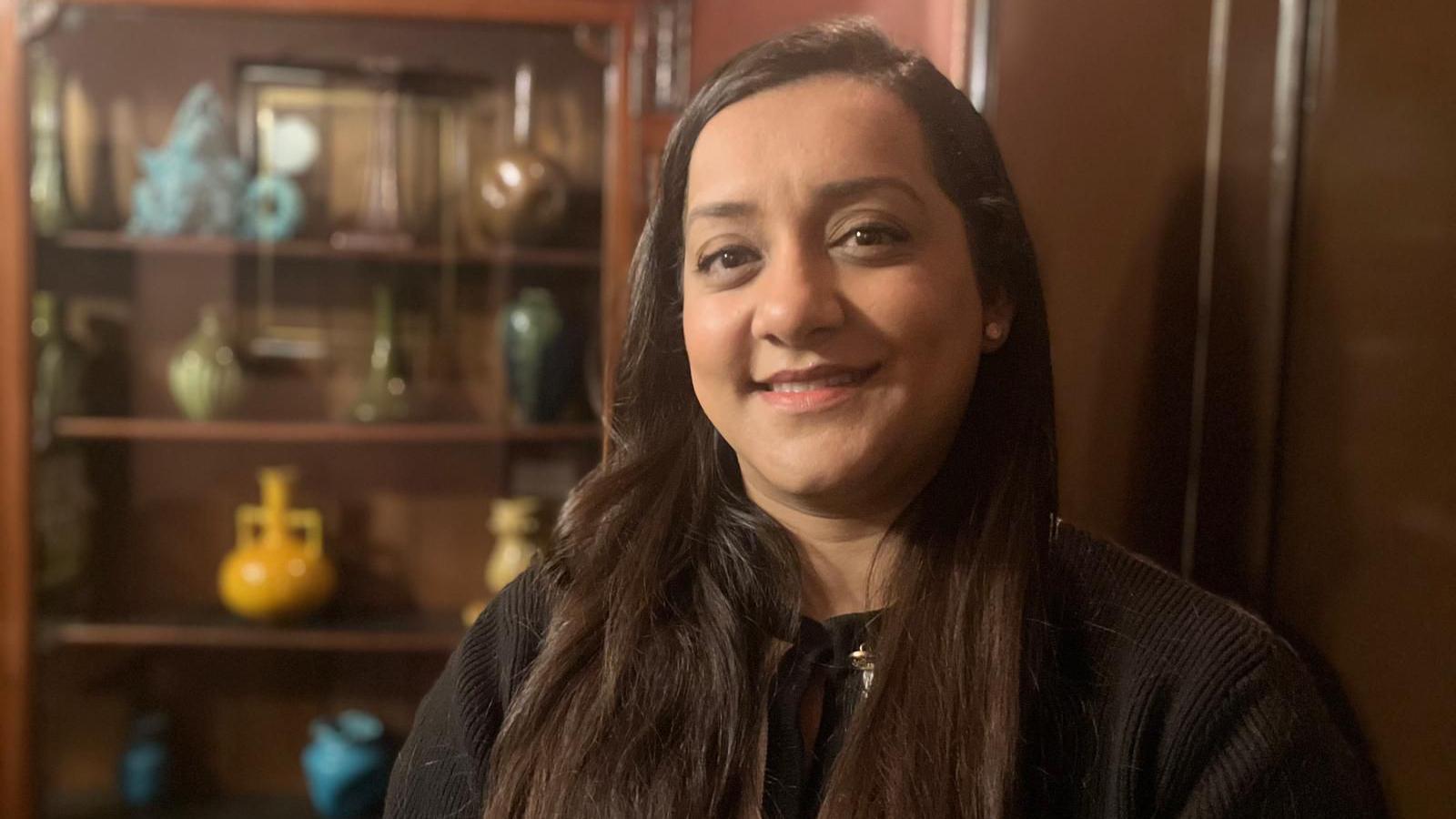 Salma Arif stands in front of a shelf full of Burmantofts pottery 