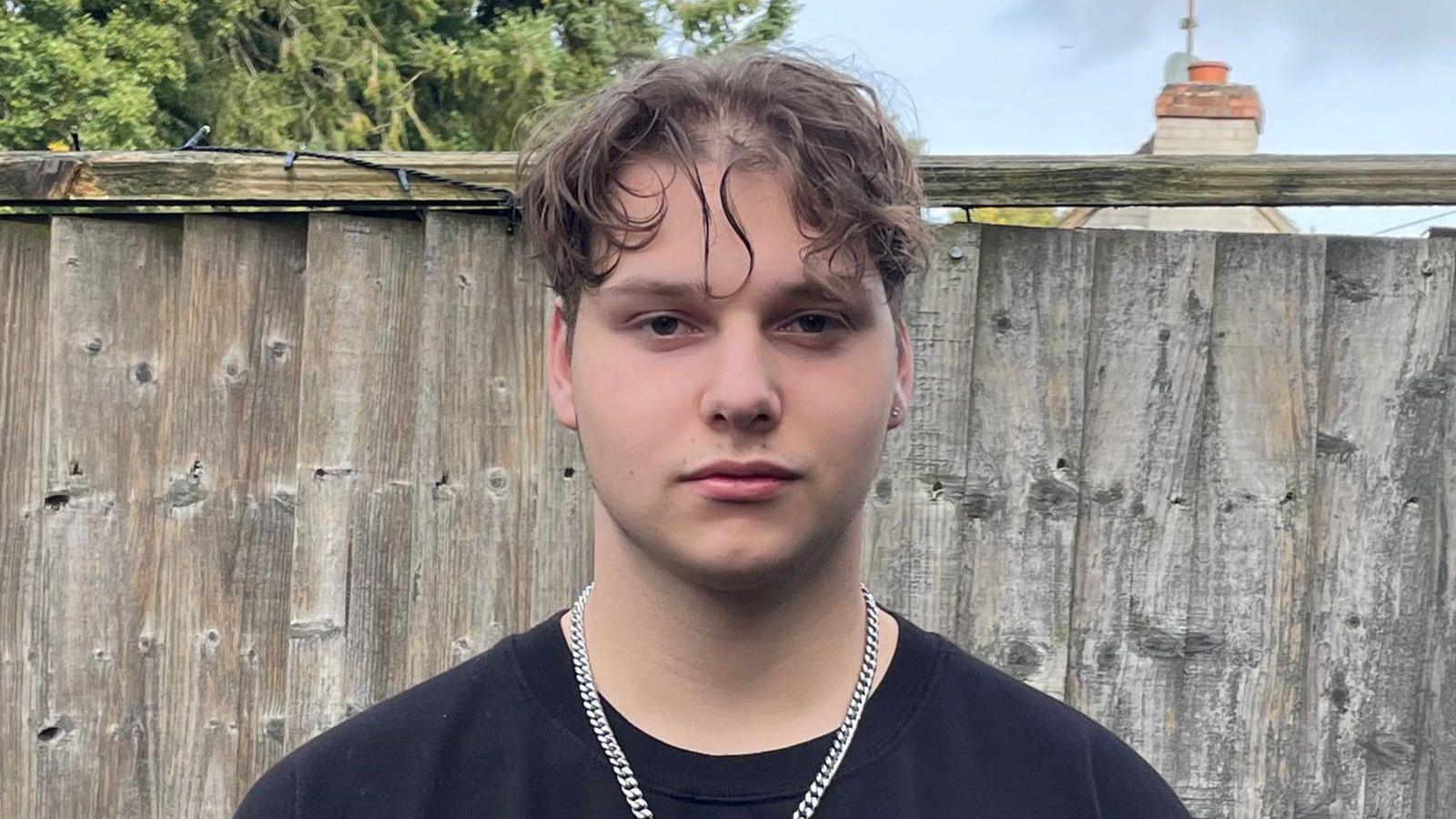 A teenager wearing a silver chain and wearing a black jumper