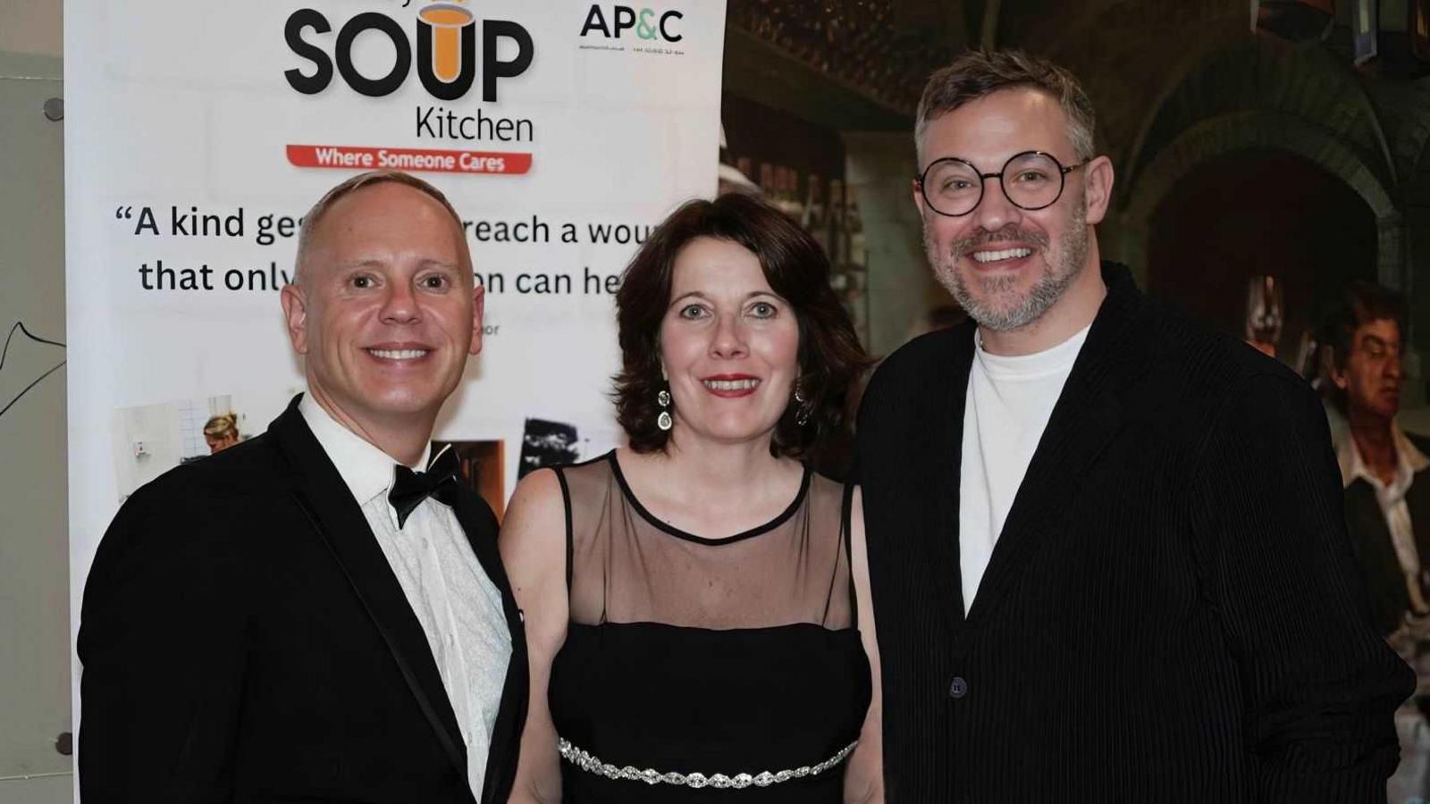 (L-R) Rob Rinder smiling at the camera is wearing a black dress suit and bow tie, Newbury Soup Kitchen chief executive Meryl Praill is smiling at the camera wearing a black evening dress and Will Young is smiling and wearing a white t-shirt and black cardigan.