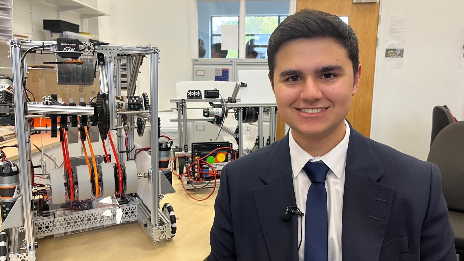 Kieran in a suit and tie sat next to a robot on a table.