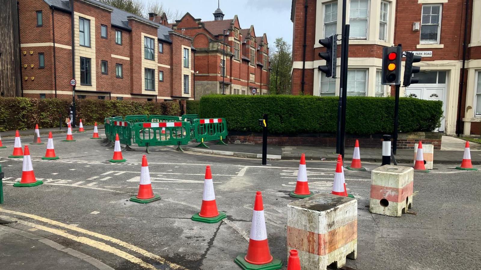 Traffic cones and bollards on the corner of a residential road near traffic lights