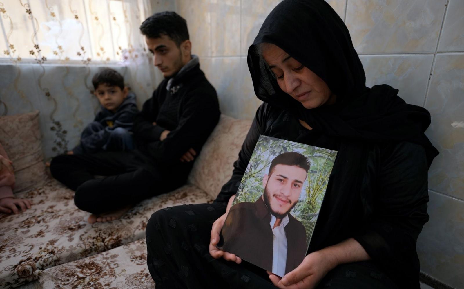 Shukria Badar looking sad sitting on a sofa with a young boy and young man while holding up a portrait of her son Baryar Mohamed, who died while crossing the Channel.