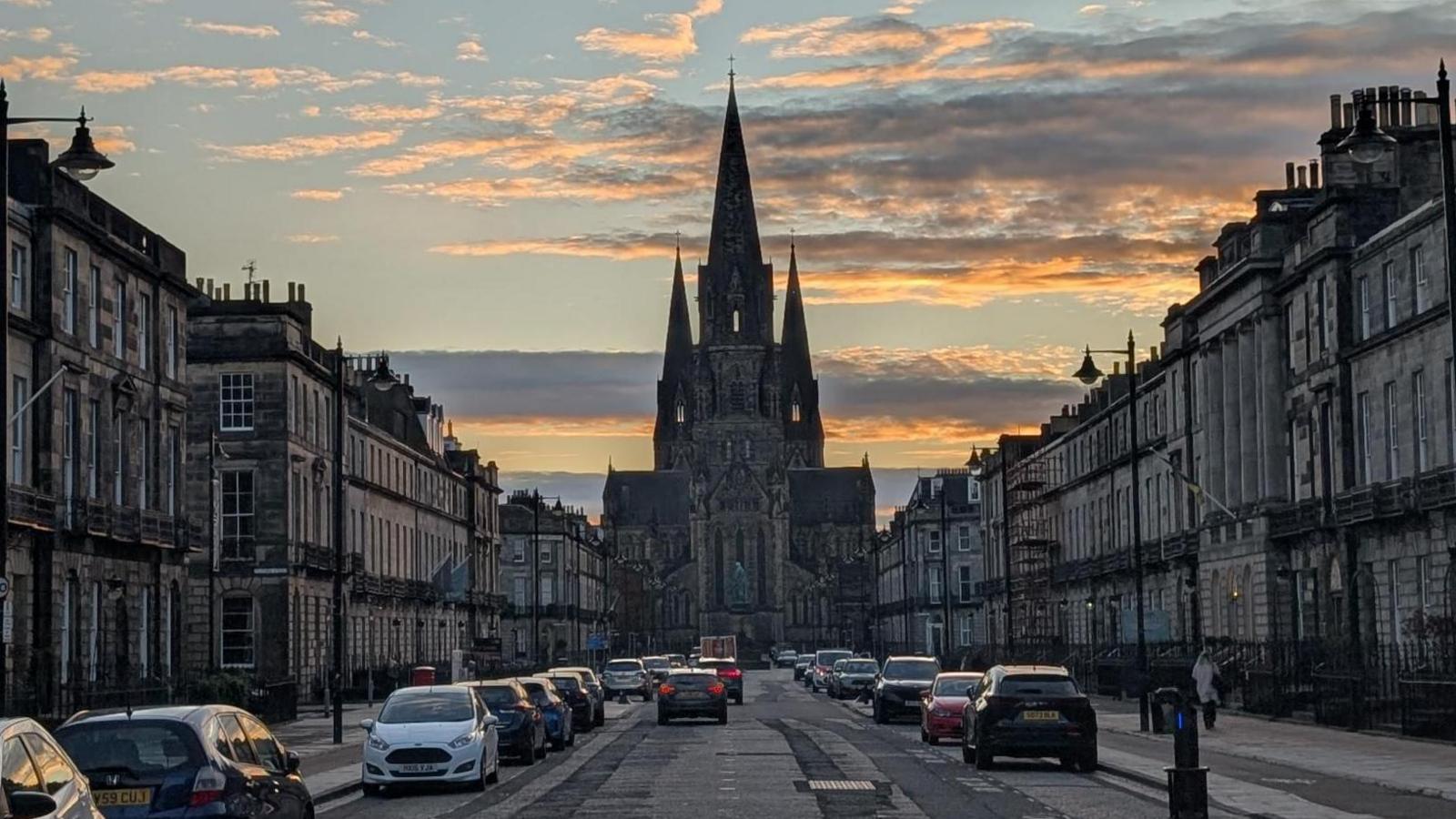 There are buildings on either side of the street. At the far end is the church with three steeples. There are also cars on the road.
