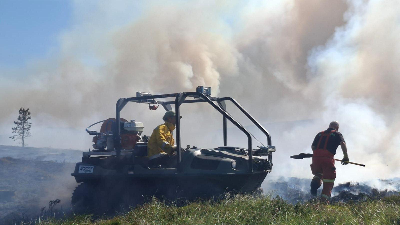 A man in an all-terrain vehicle and another man with with spade work to put out flames