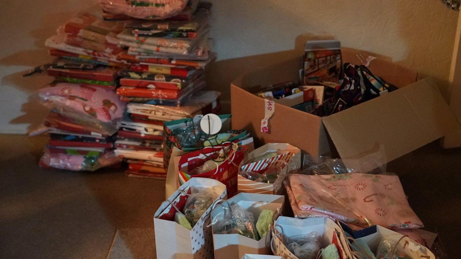 The Christmas bedding packs are piled high on the carpeted living room floor. There are also dozens of pyjama sets piled in a cardboard box and filled Christmas gift bags too.