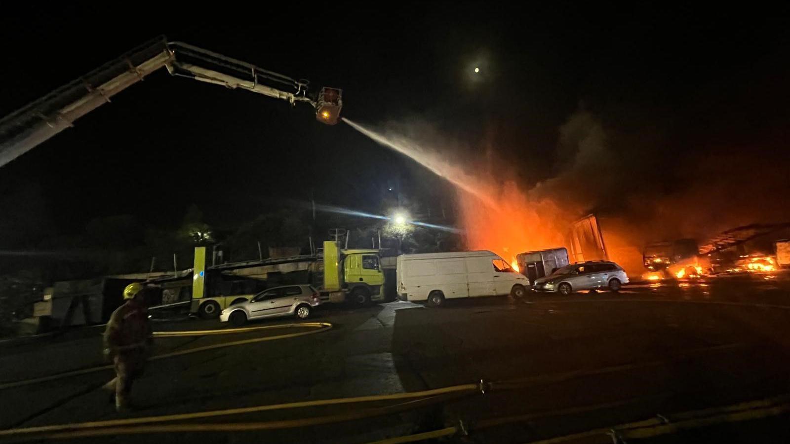 Fire officers using an aerial platform shoot water onto a large fire at night time 